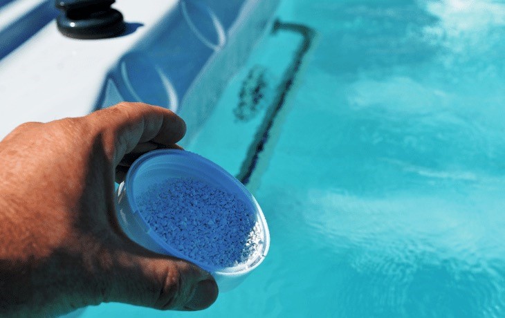 Person holding a scoop of spa chemicals over hot tub water.