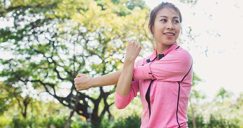 Person stretching an arm outdoors.