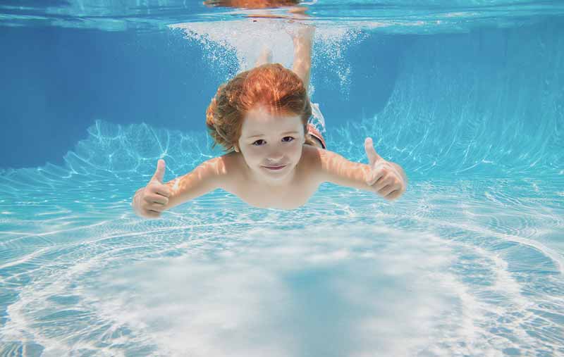 Child swimming underwater giving thumbs up