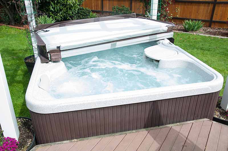 Outdoor hot tub with bubbling water and a partially opened cover