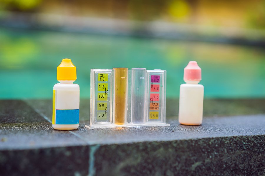 pool water test kit and reagent bottles placed beside a swimming p