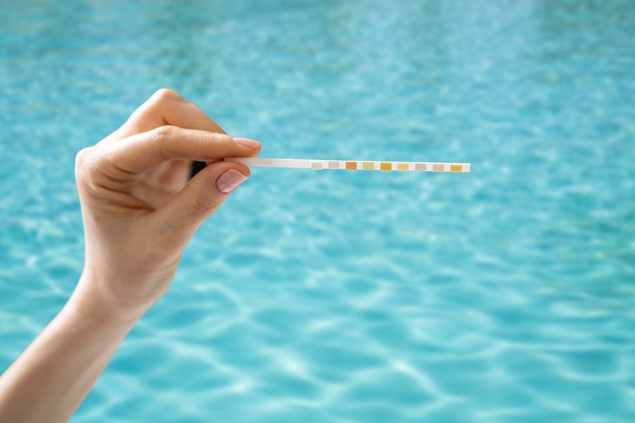 Hand holding a water test strip over a pool.